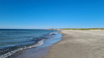 A beach with a clear sky, calm sea, and a distant lighthouse.