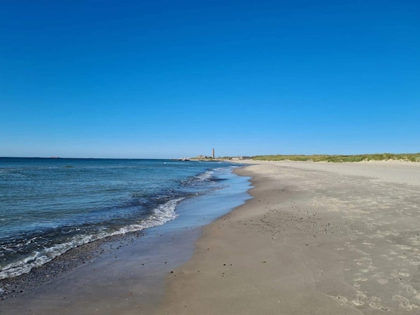 A beach with a clear sky, calm sea, and a distant lighthouse.