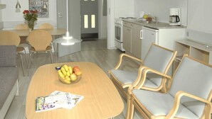 Una cucina moderna con mobili bianchi, un'area pranzo con tavolo e sedie in legno, e un soggiorno con divano.
