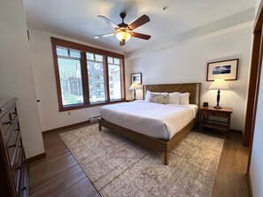 A bedroom with a bed, a nightstand, a ceiling fan, a window with blinds, and a framed picture on the wall. - Updated, Village Corner Condo! Parking, Pool & Spa (Mammoth Lakes)