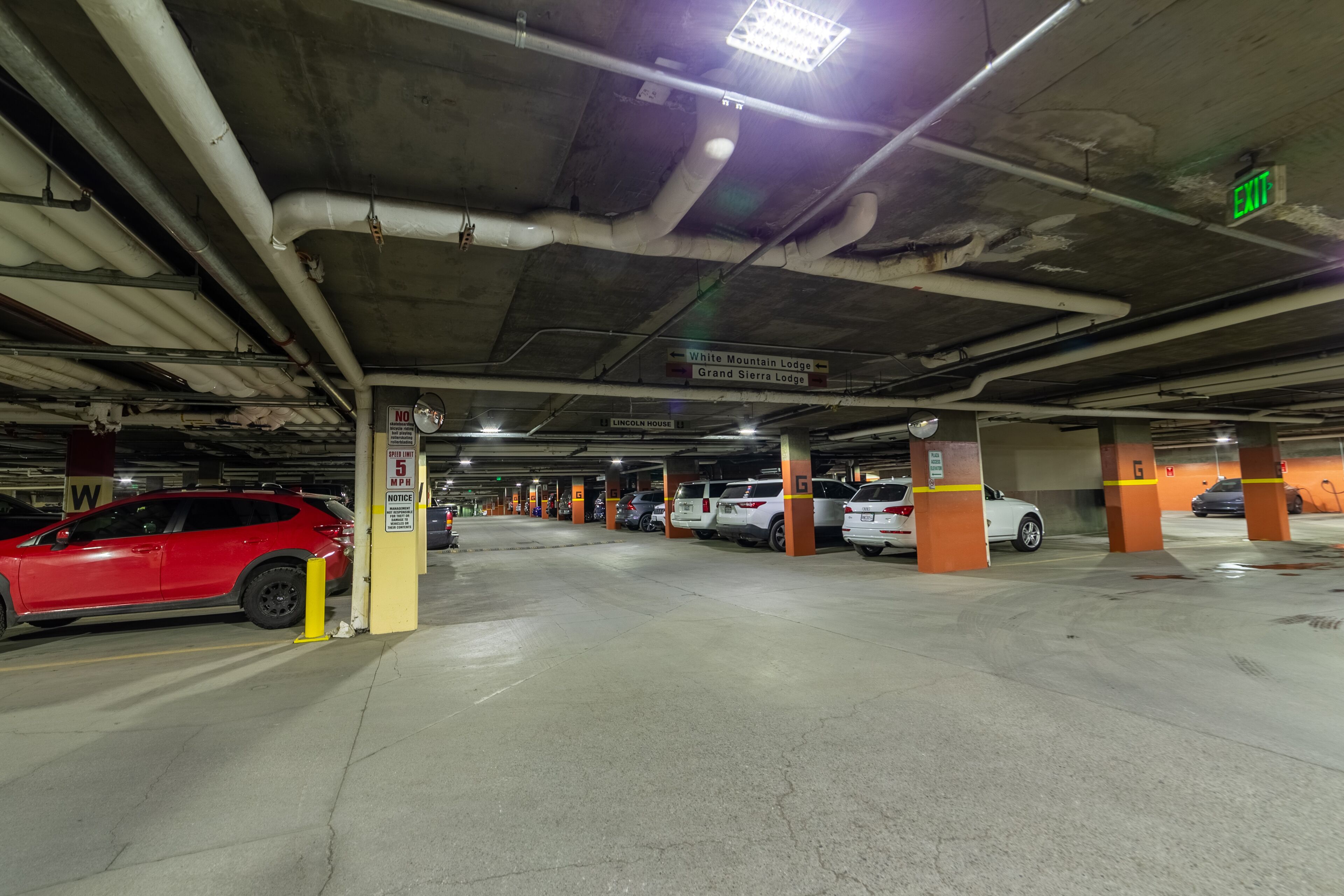 An underground parking garage with multiple levels, marked parking spaces, and directional signs for lodges.