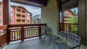 Un balcon doté de balustrades en bois, de chaises en métal et offrant une vue sur des bâtiments rouges et de la verdure.