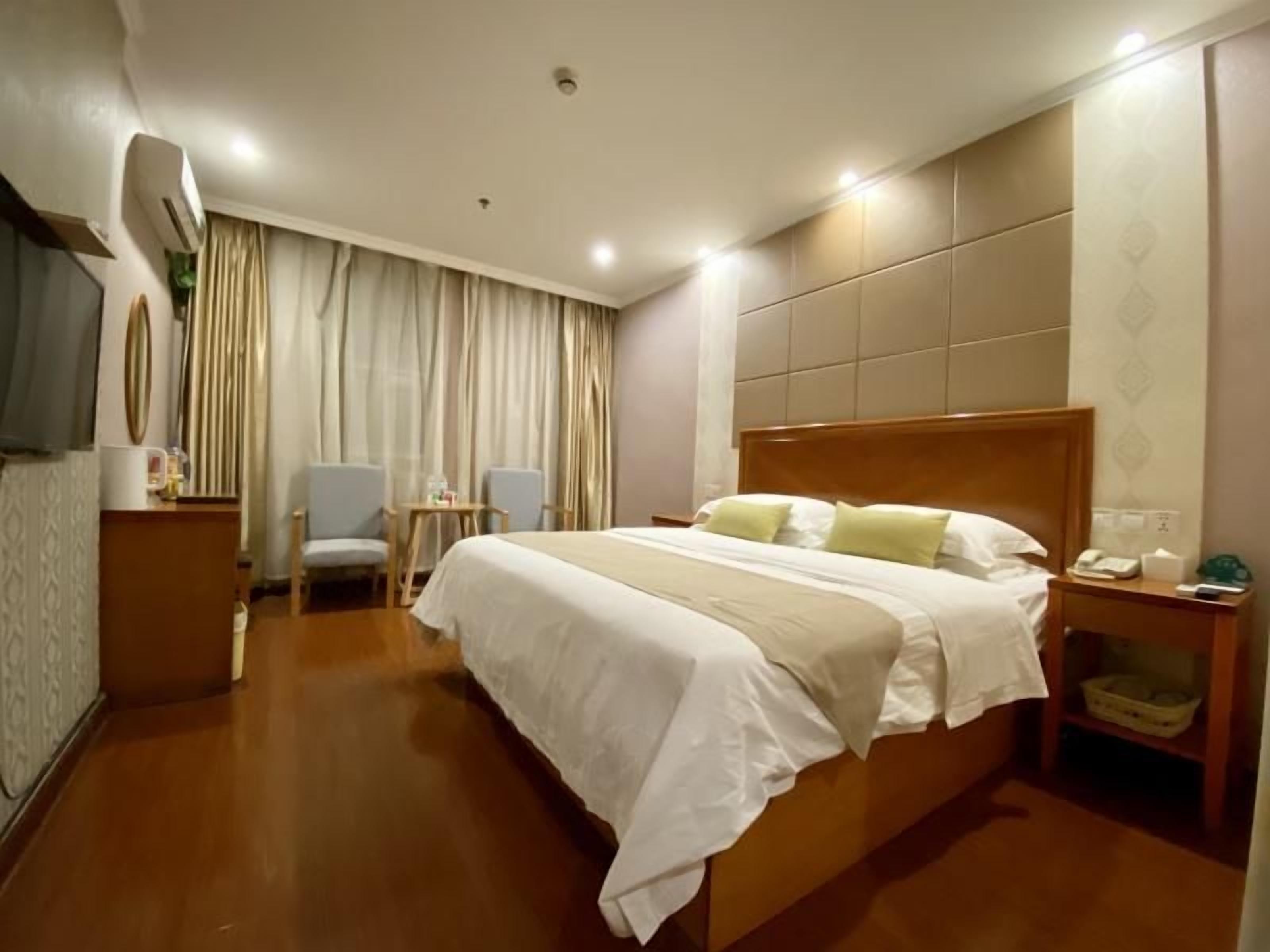 A hotel room with a large bed, a desk with a chair, a television, and a window with curtains.