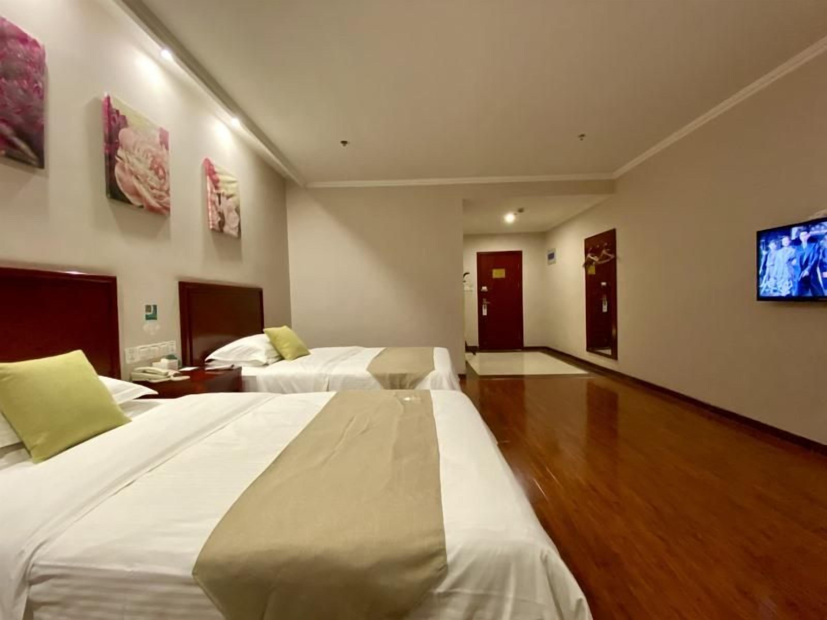 Habitación de hotel con dos camas, un televisor y un pasillo que lleva a una puerta.