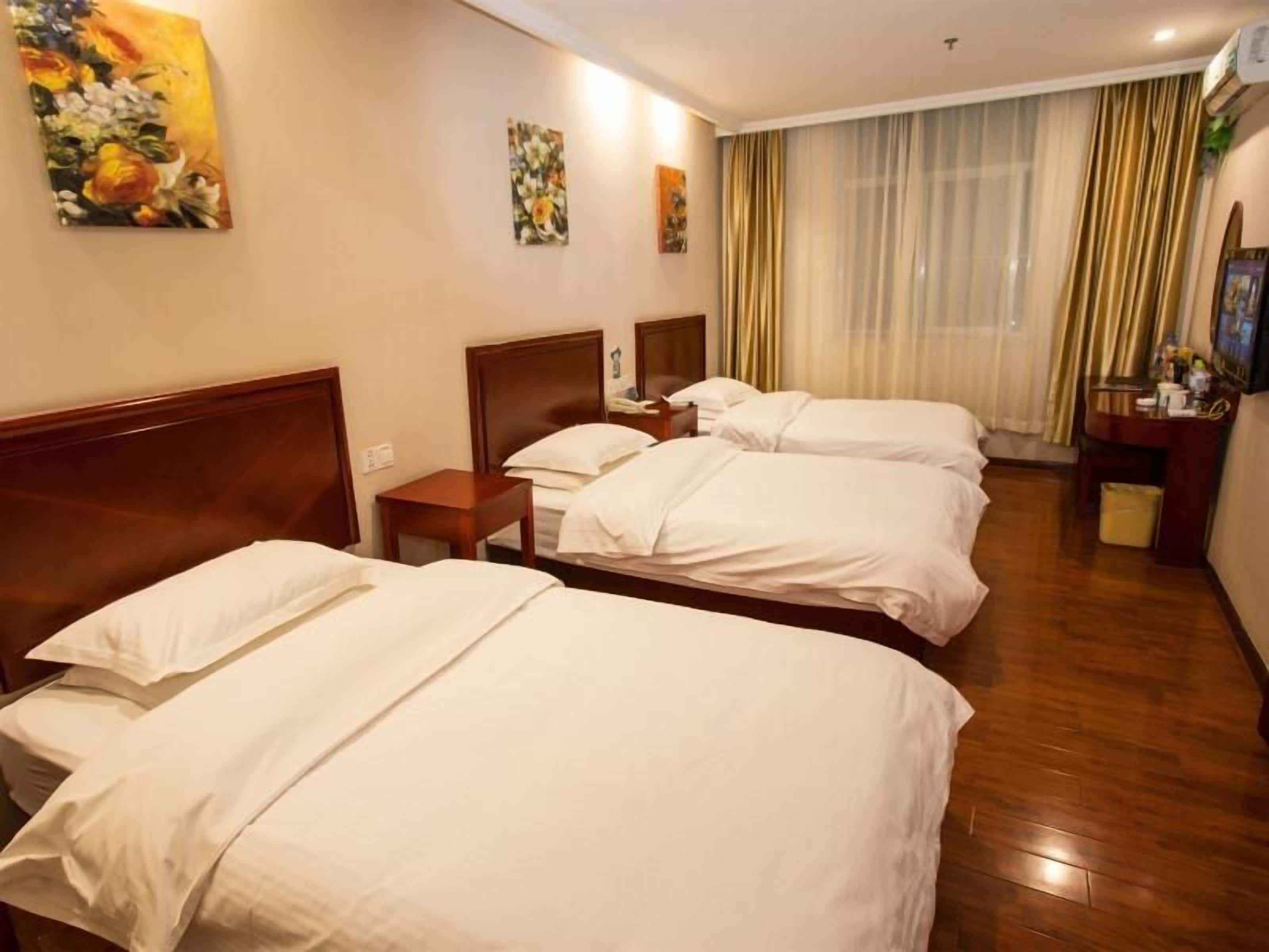 A hotel room with three beds, wooden flooring, and a large window with curtains.