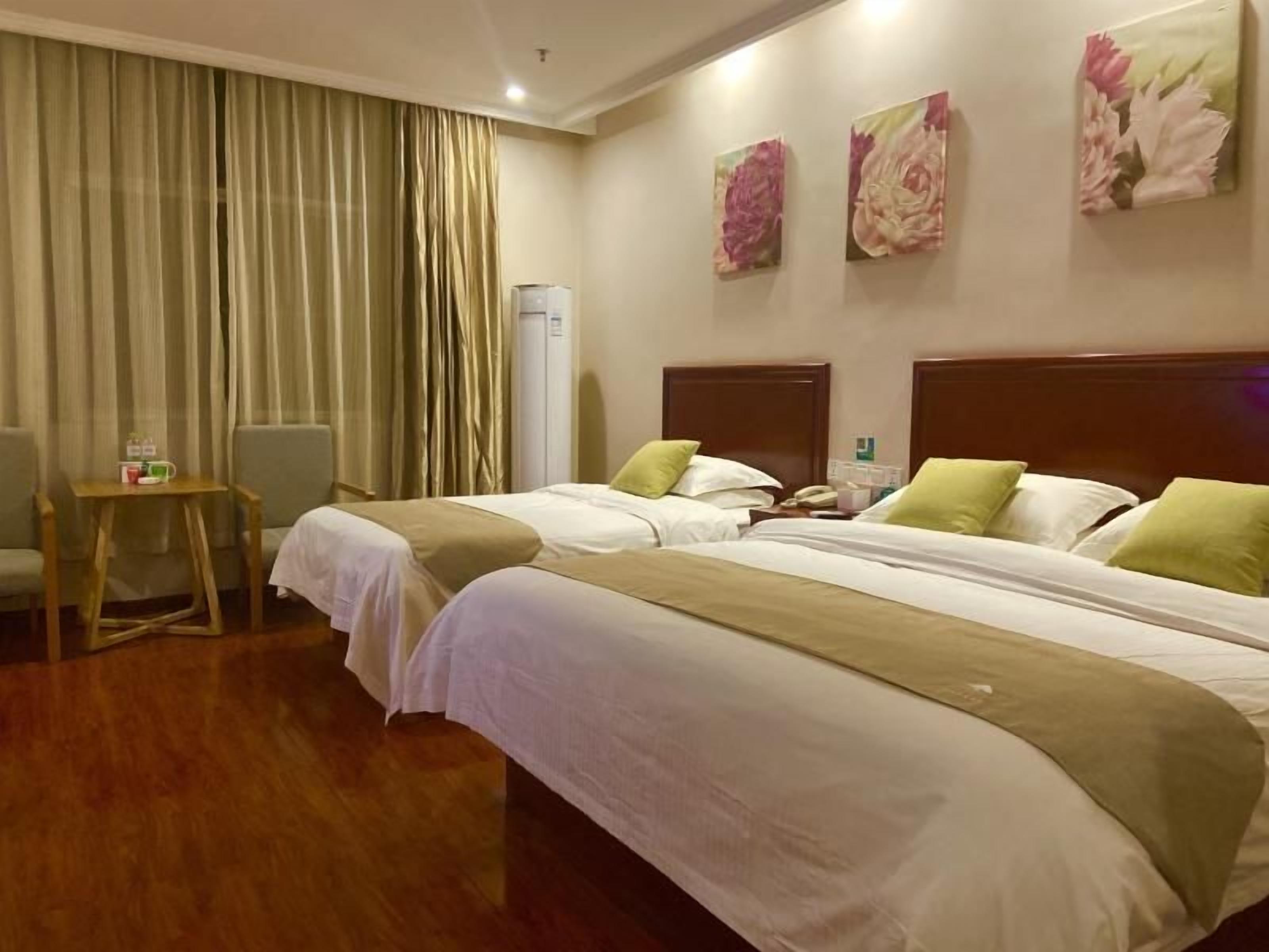 Quarto de hotel com duas camas, uma mesinha com uma cadeira e uma janela grande com cortinas.