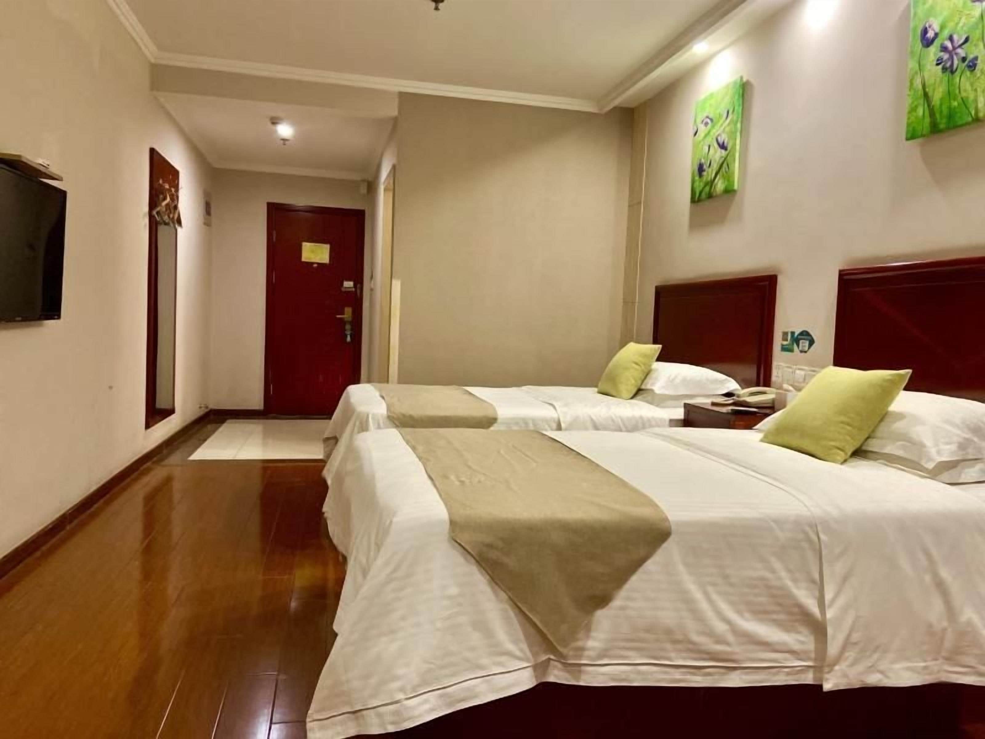 A hotel room with two beds, a wooden floor, a red door, and a painting on the wall.