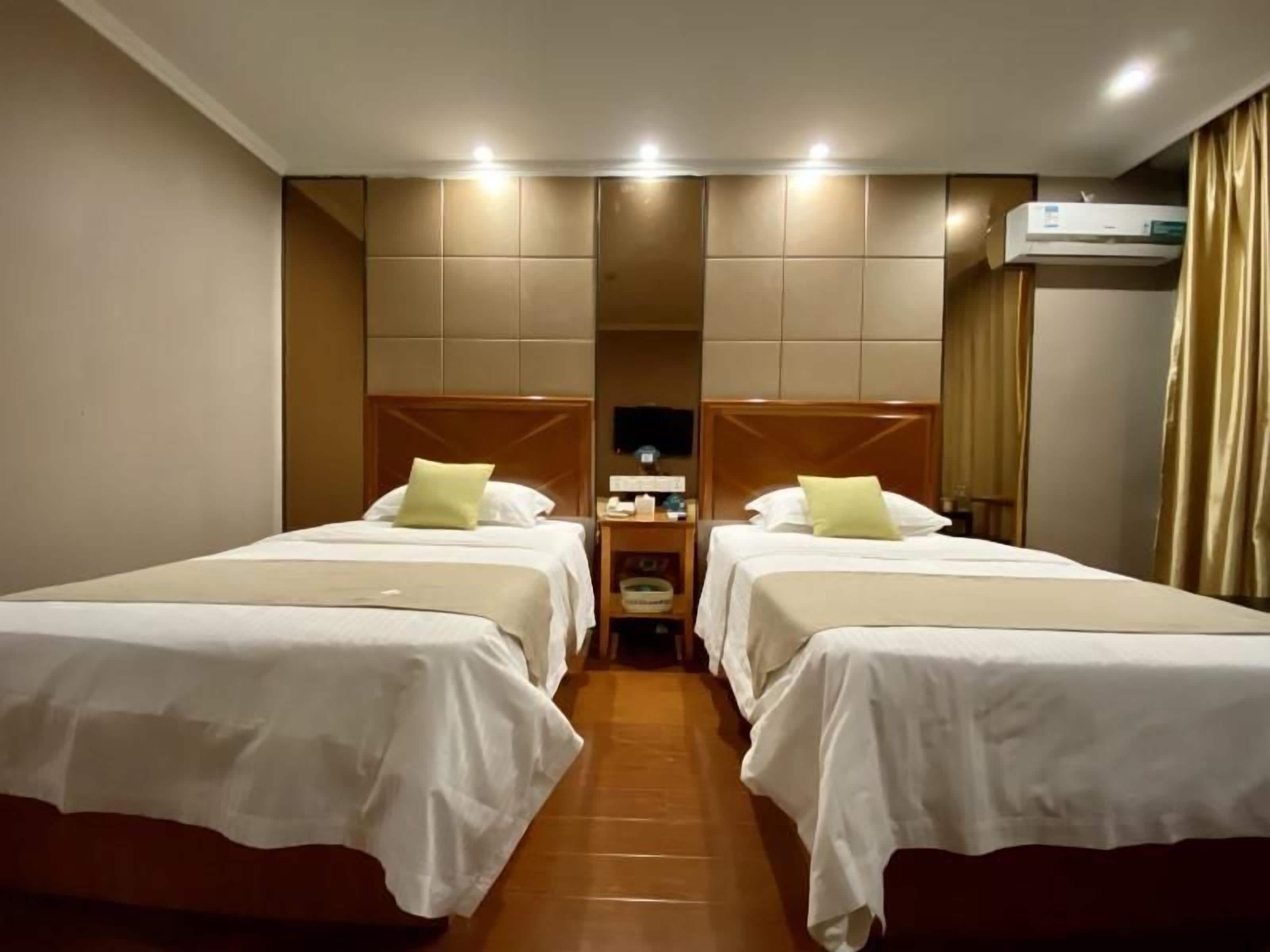 A hotel room with two beds, a nightstand, and an air conditioning unit.