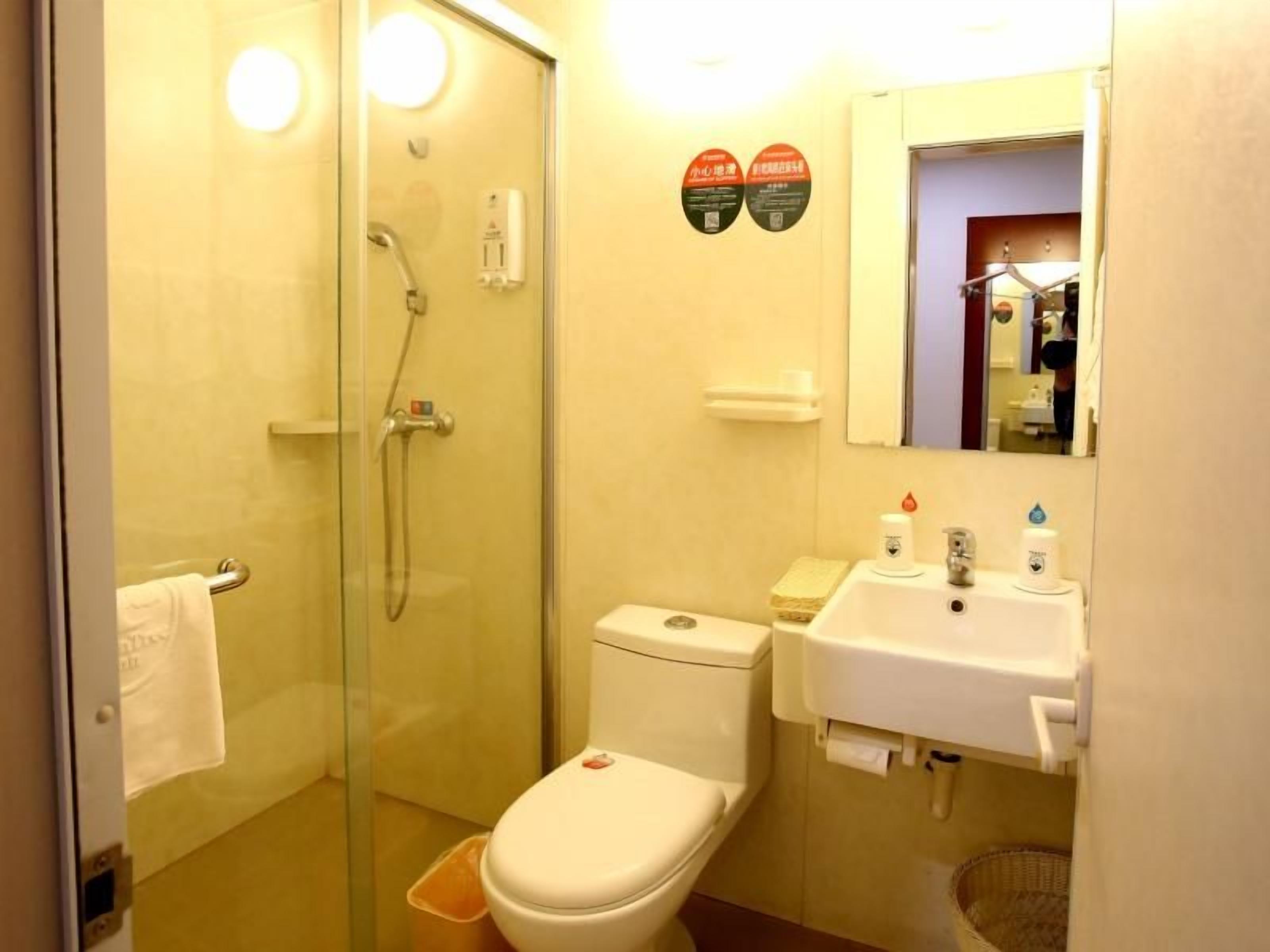 A small bathroom with a glass-enclosed shower, a toilet, and a sink with a mirror above it.