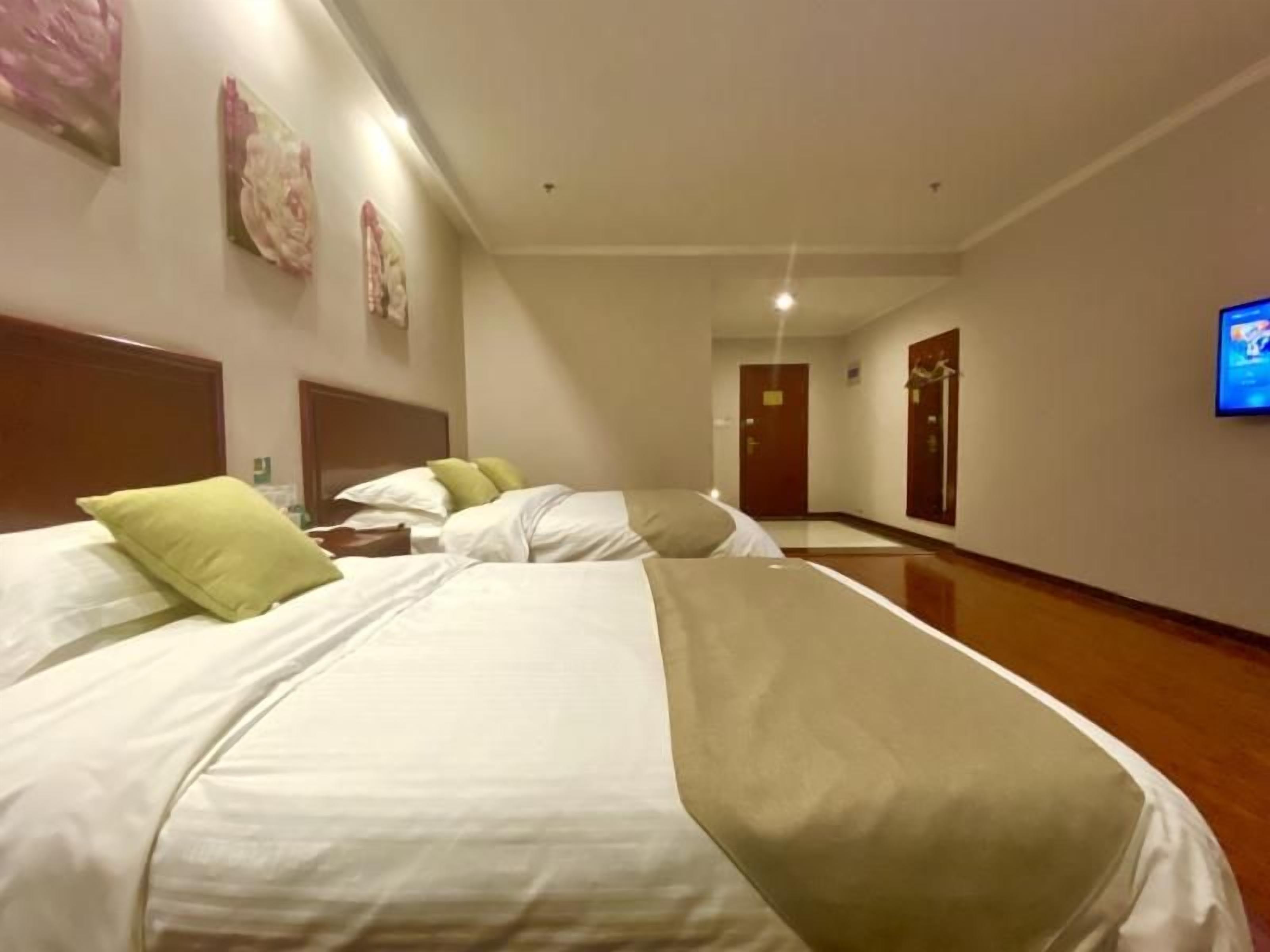A hotel room with two beds, each with white linens and green pillows. There is a television mounted on the wall to the right.