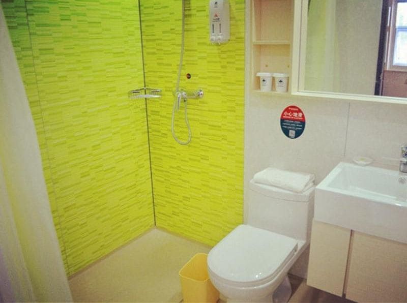 Un baño con pared de azulejos amarillos, inodoro blanco, lavamanos y zona de ducha.
