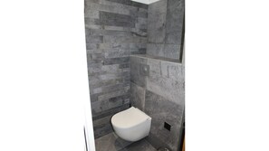 Bathroom features a minimalist design with a textured appearance, a toilet, and a vent.