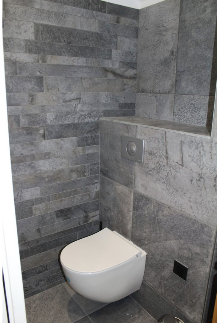 A bathroom with a white toilet and grey stone tiles.