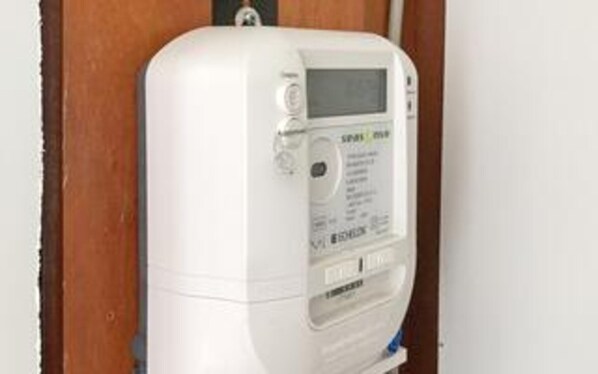 Un termostato bianco fissato alla parete, con display digitale e pulsanti di controllo, e il marchio.