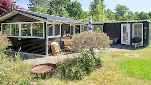 Une cabane dotée d’un porche couvert, d’une porte-fenêtre coulissante et d’un petit espace extérieur aménagé pour s’asseoir.