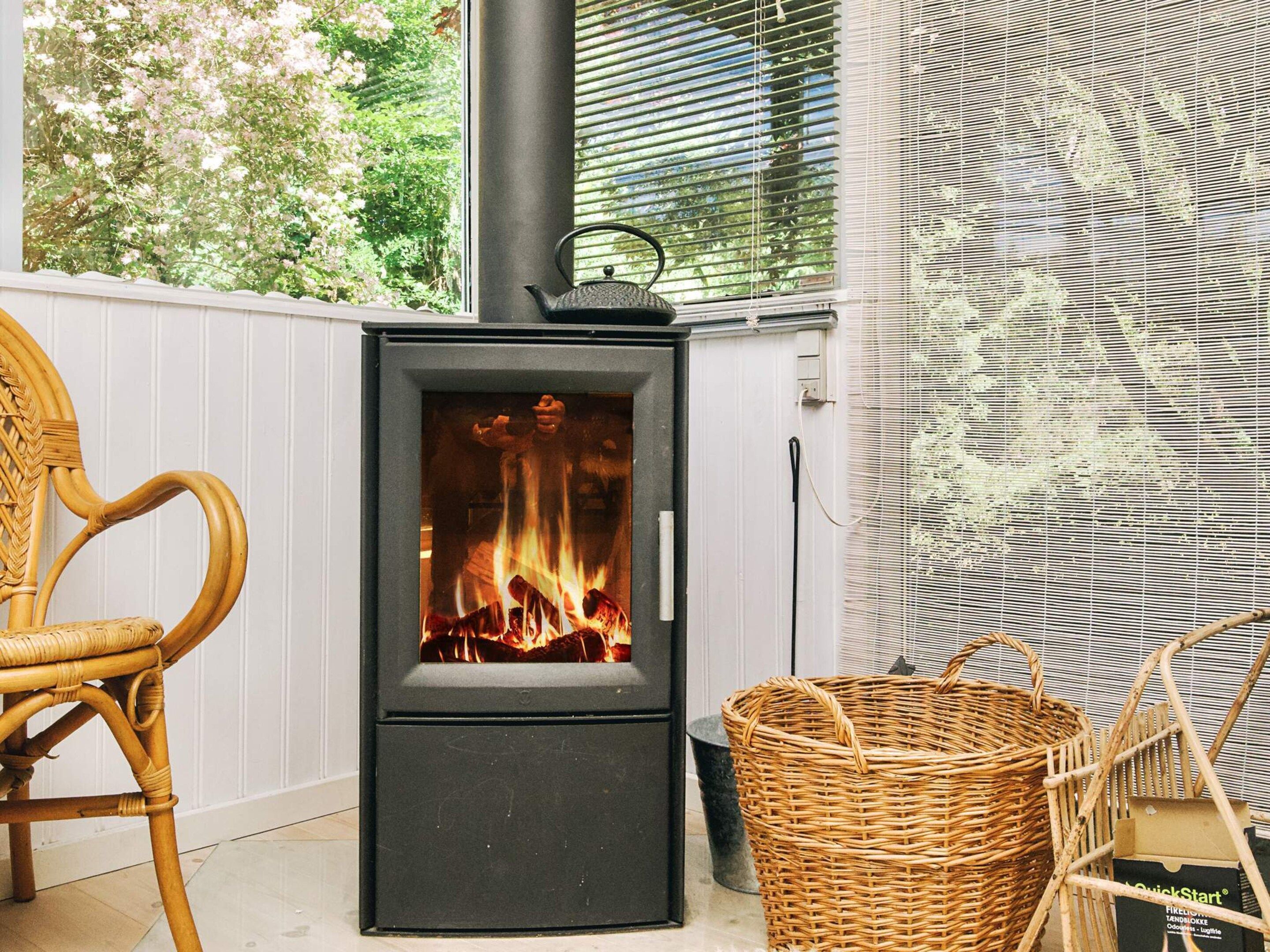 A wood-burning stove with a visible fire, a wicker chair, and a basket.