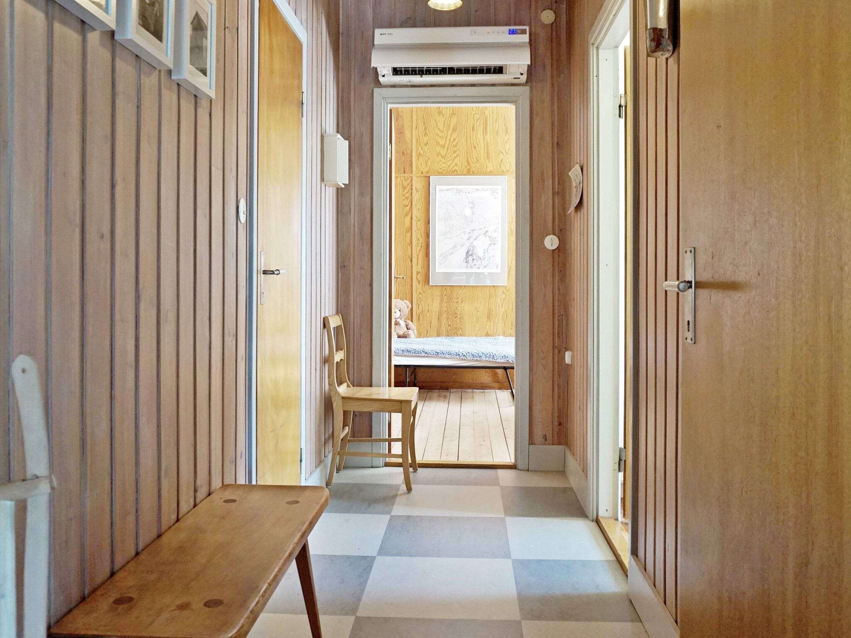 A hallway with a wooden bench, a door with a window, and a wall-mounted air conditioner.