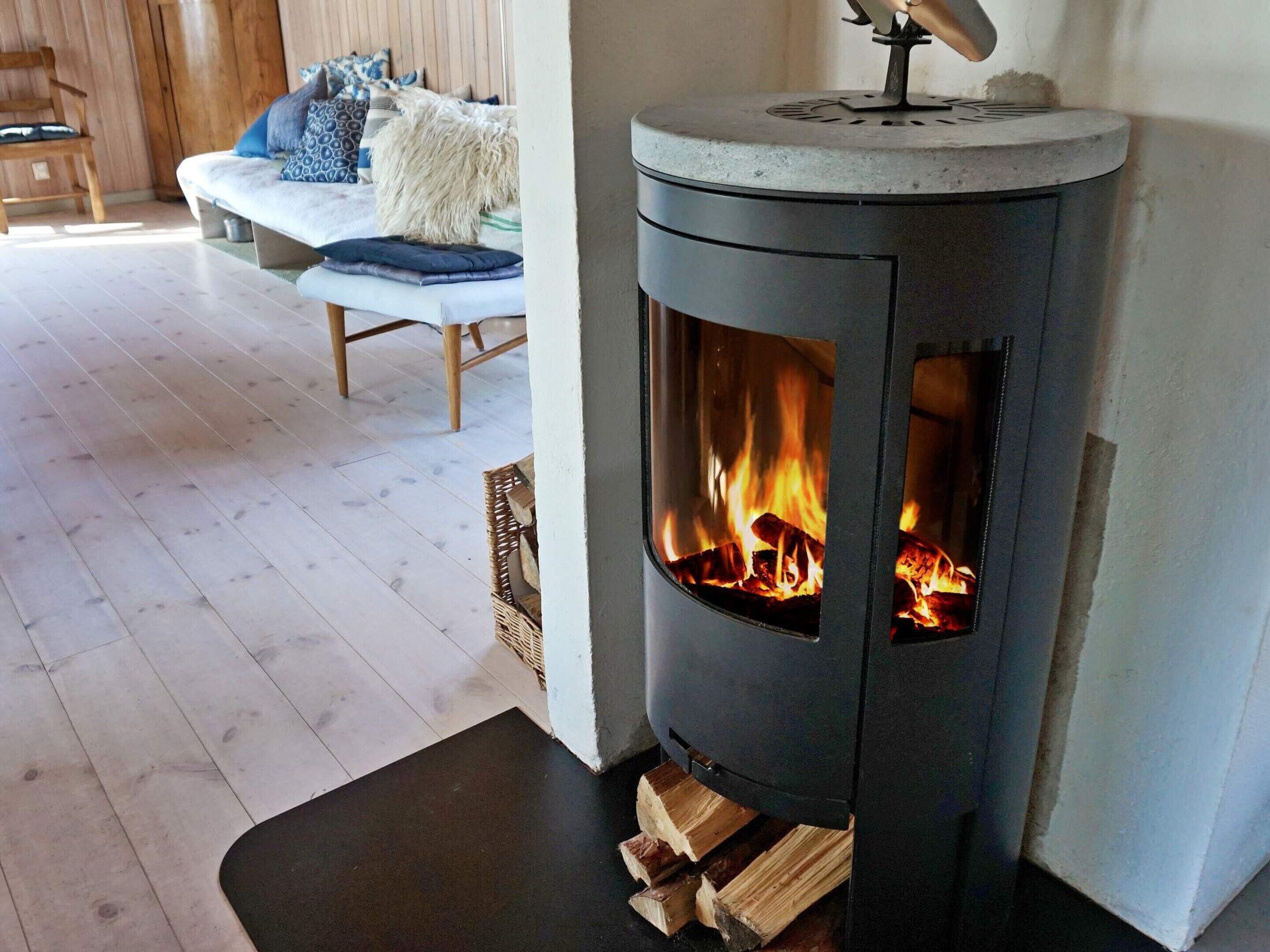 A wood-burning stove with visible flames, a wooden chair, a bench with cushions, and a wooden floor.