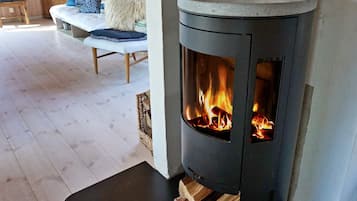 A wood-burning stove with visible flames, a wooden chair, a bench with cushions, and a wooden floor.