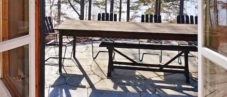 A wooden deck with a picnic table and benches, surrounded by trees and a snowy landscape.