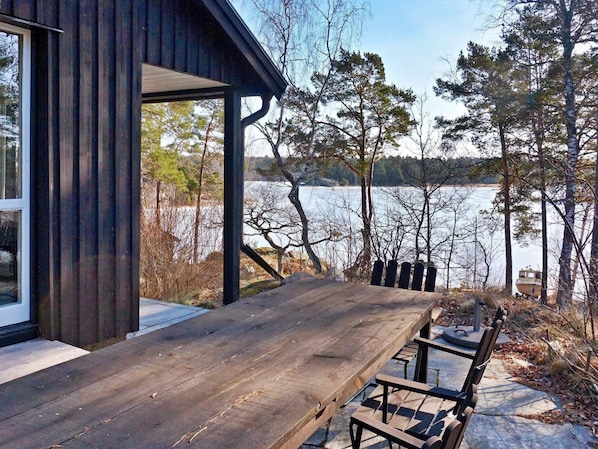 A wooden deck with a table and chairs overlooking a lake, surrounded by trees.