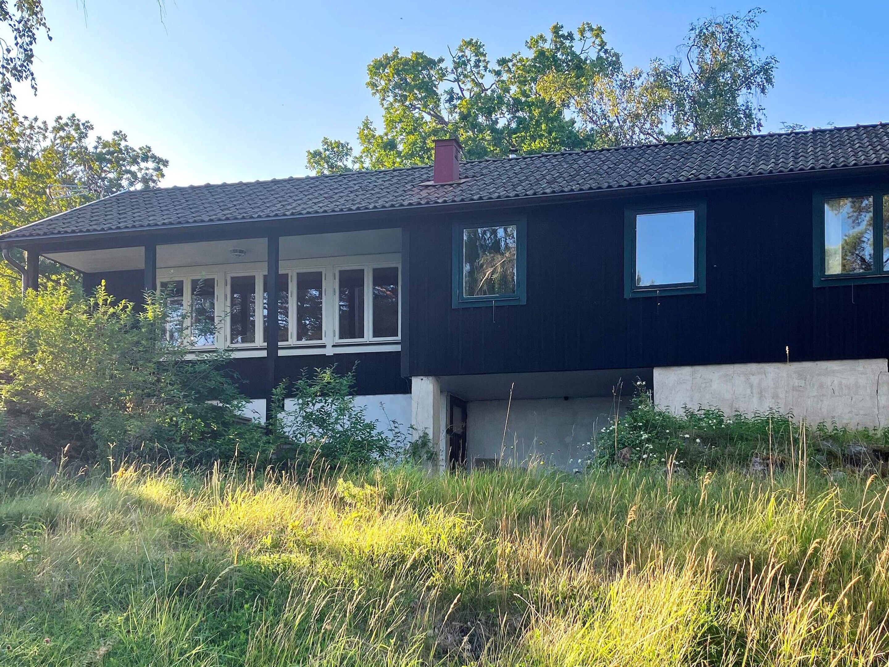 A two-story house with a balcony, surrounded by tall grass and trees.