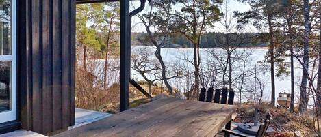 A wooden deck with a table and chairs overlooking a lake, surrounded by trees.