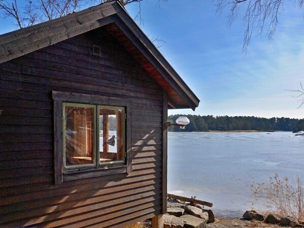 Una cabaña de madera con ventana y vista a un lago helado.
