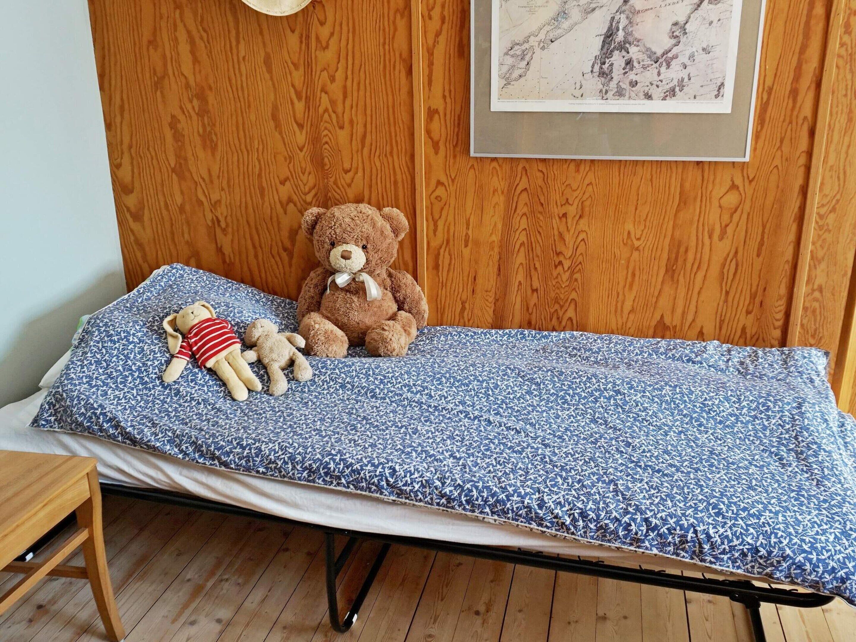 A single bed with a patterned blue cover, a wooden headboard, and a framed map on the wall.