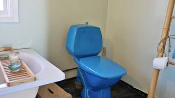 A bathroom with a white bathtub, a blue toilet, a wooden stool, and a bamboo ladder.