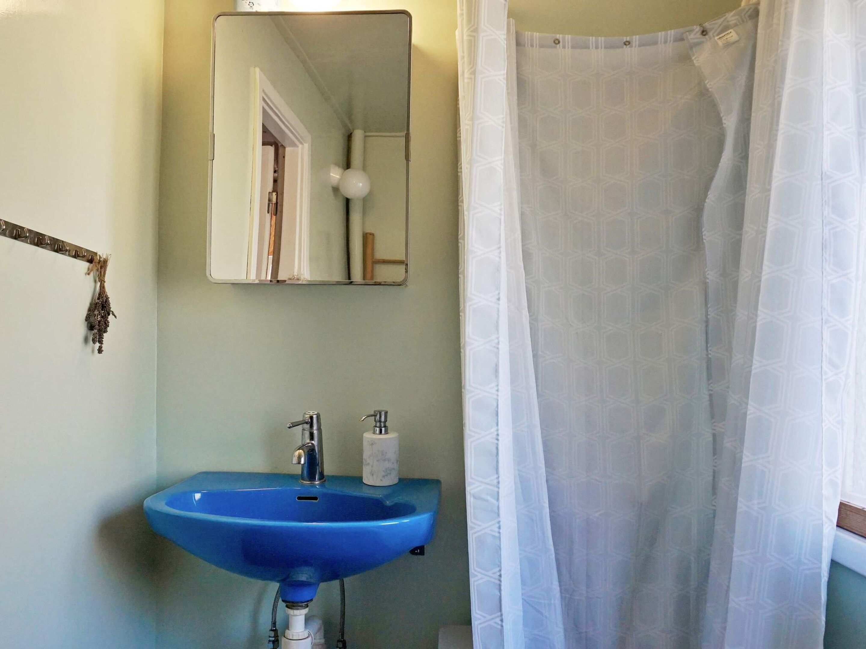 A bathroom with a blue sink, a mirror, a shower curtain, and a towel rack.