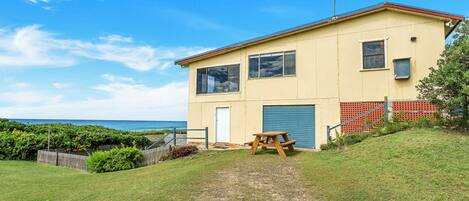A two-story building with a garage, a picnic table, and a view of the ocean.