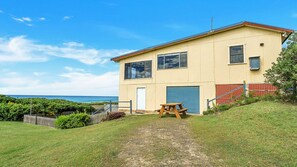 A two-story building with a garage, a picnic table, and a view of the ocean.