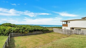 A modern two-story house with a large backyard, a wooden fence, and a view of the ocean.