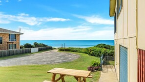 A residential property with a paved driveway, a wooden picnic table, and a view of the ocean.