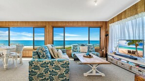 A spacious living room with a large window overlooking a beach, furnished with a sofa, chairs, and a coffee table. - Kokomo - Charming Coastal Escape (Wooli)