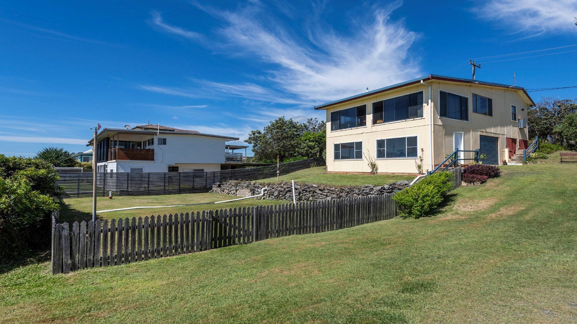 A two-story house with a fenced yard, a wooden deck, and a stone wall.
