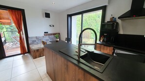 A modern kitchen with a built-in island, stainless steel sink, and a microwave. - L'Arveysan (Sainte-Marie-d'Alvey)