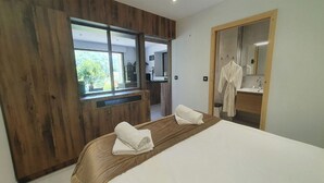 A modern bedroom with a large bed, wooden wardrobe, a mirror, and a view of the kitchen. - L'Arveysan (Sainte-Marie-d'Alvey)