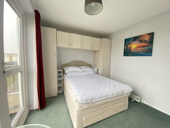Une chambre à coucher avec un lit, une armoire, un tableau et une fenêtre avec des rideaux.