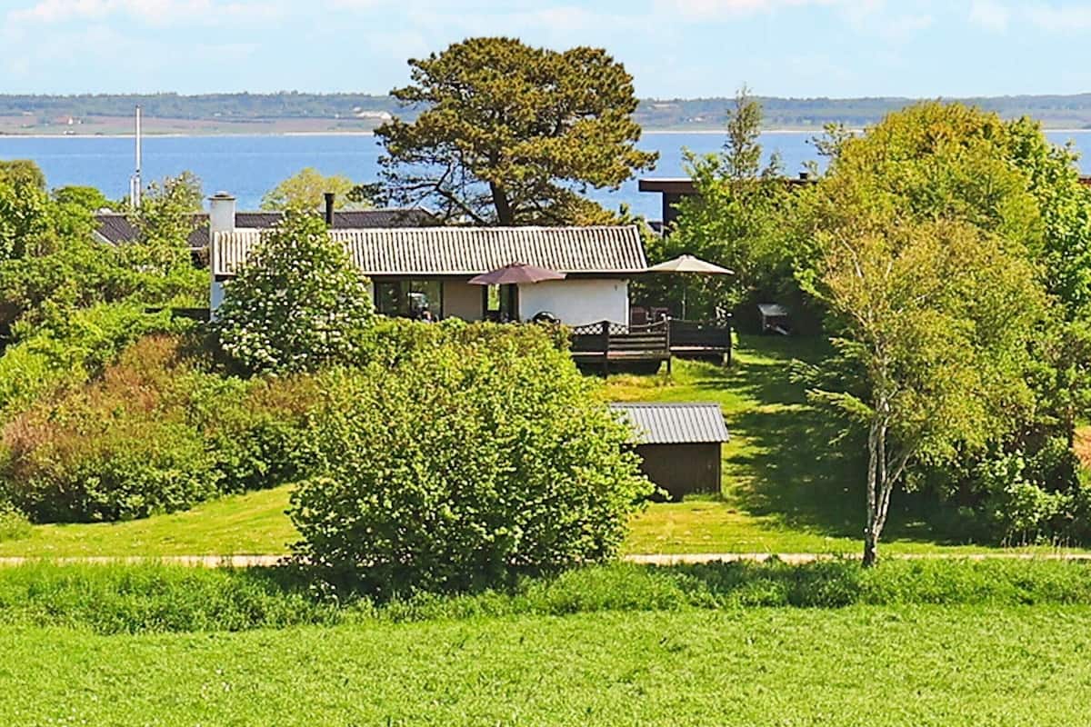 A house with a large tree in front, a deck, and a view of the water.