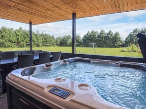 A hot tub with a control panel, surrounded by outdoor furniture and a wooden pergola.