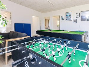 A room with a foosball table, a pool table, and a sofa. There are framed pictures on the wall and a blue cabinet.