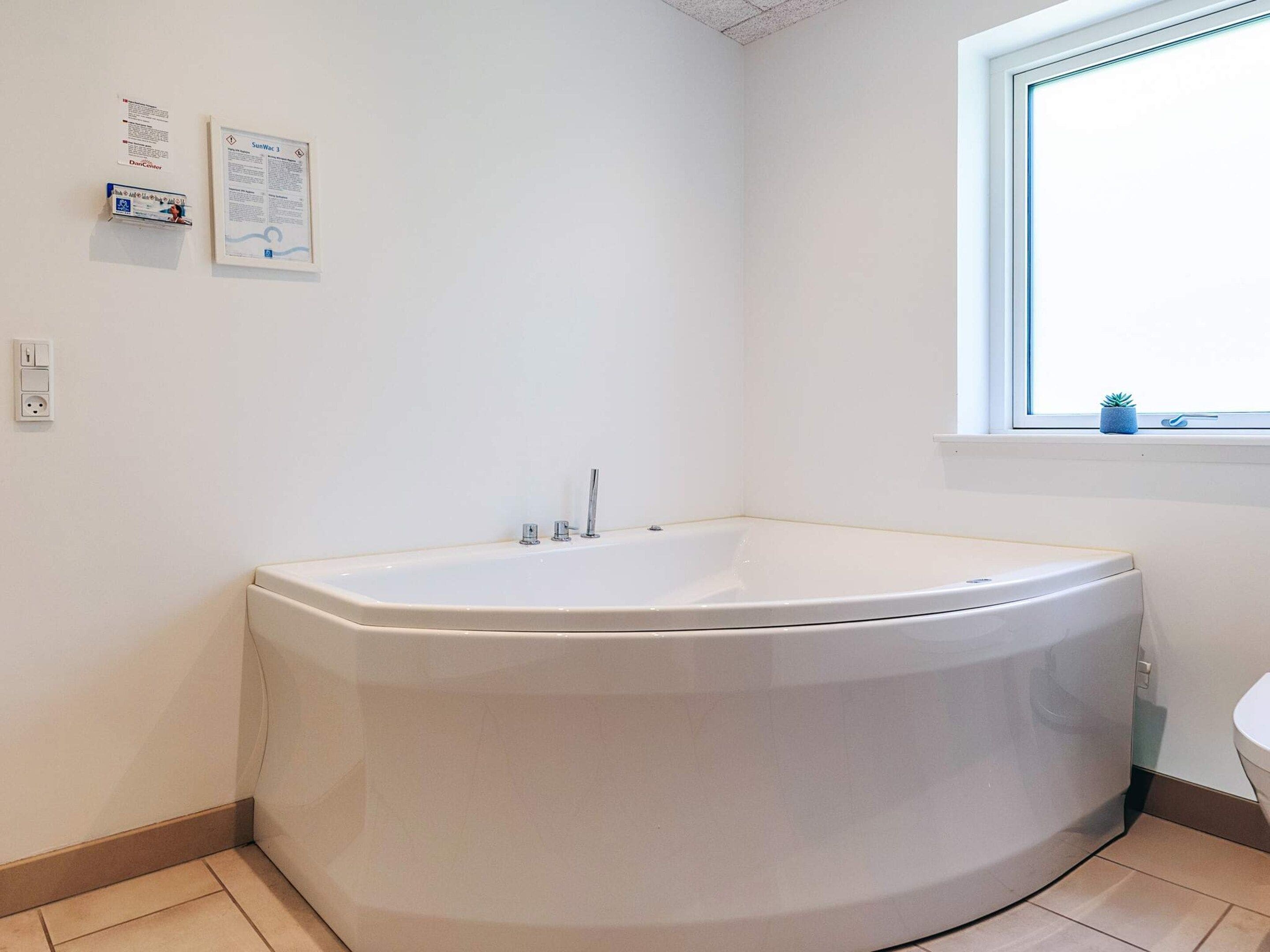A modern bathroom with a freestanding bathtub, a window, and a small potted plant.