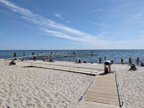 A beach with a wooden pier extending into the water, sandy beach, and clear skies.