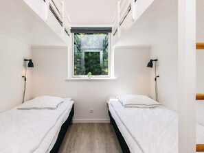 Une petite chambre moderne avec deux lits simples, une fenêtre donnant sur un paysage verdoyant et une petite plante posée sur le rebord de la fenêtre.
