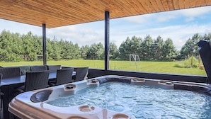 Ett bubbelbad med en kontrollpanel, omgivet av utemöbler och en träpergola.