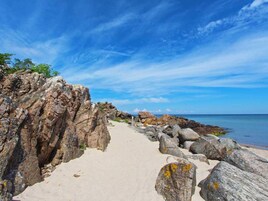 Un sentiero roccioso che costeggia la spiaggia e conduce verso il mare, con cieli sereni.