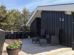 A wooden deck with outdoor furniture, a large planter with flowers, and a building with the number 34.