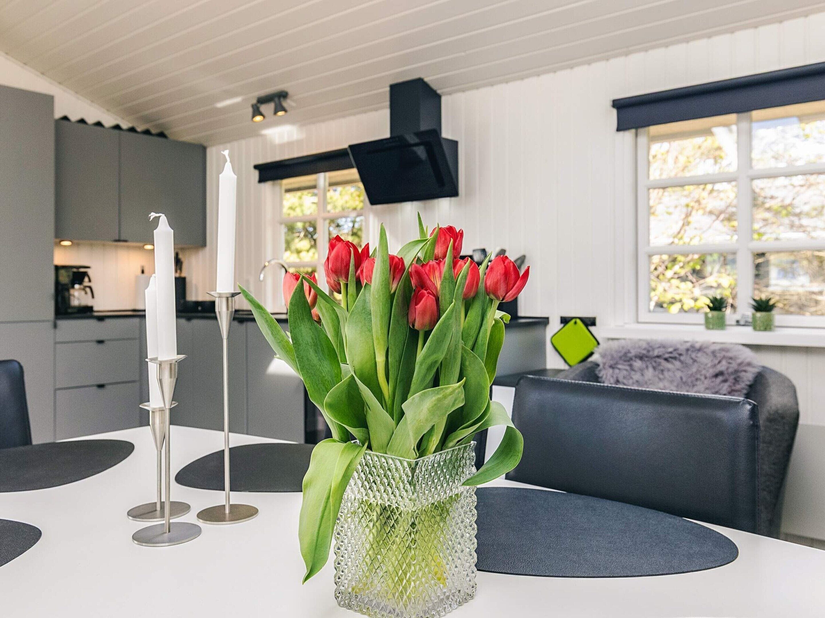 Een moderne keuken met witte kasten, een eettafel met een vaas rode tulpen, en een zwarte bank.